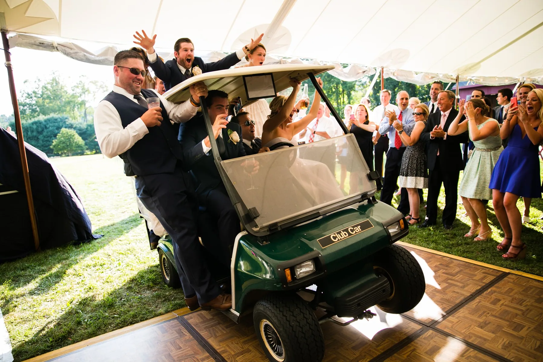 Groom and groomsmen celebrating on a golf cart as guests cheer them on