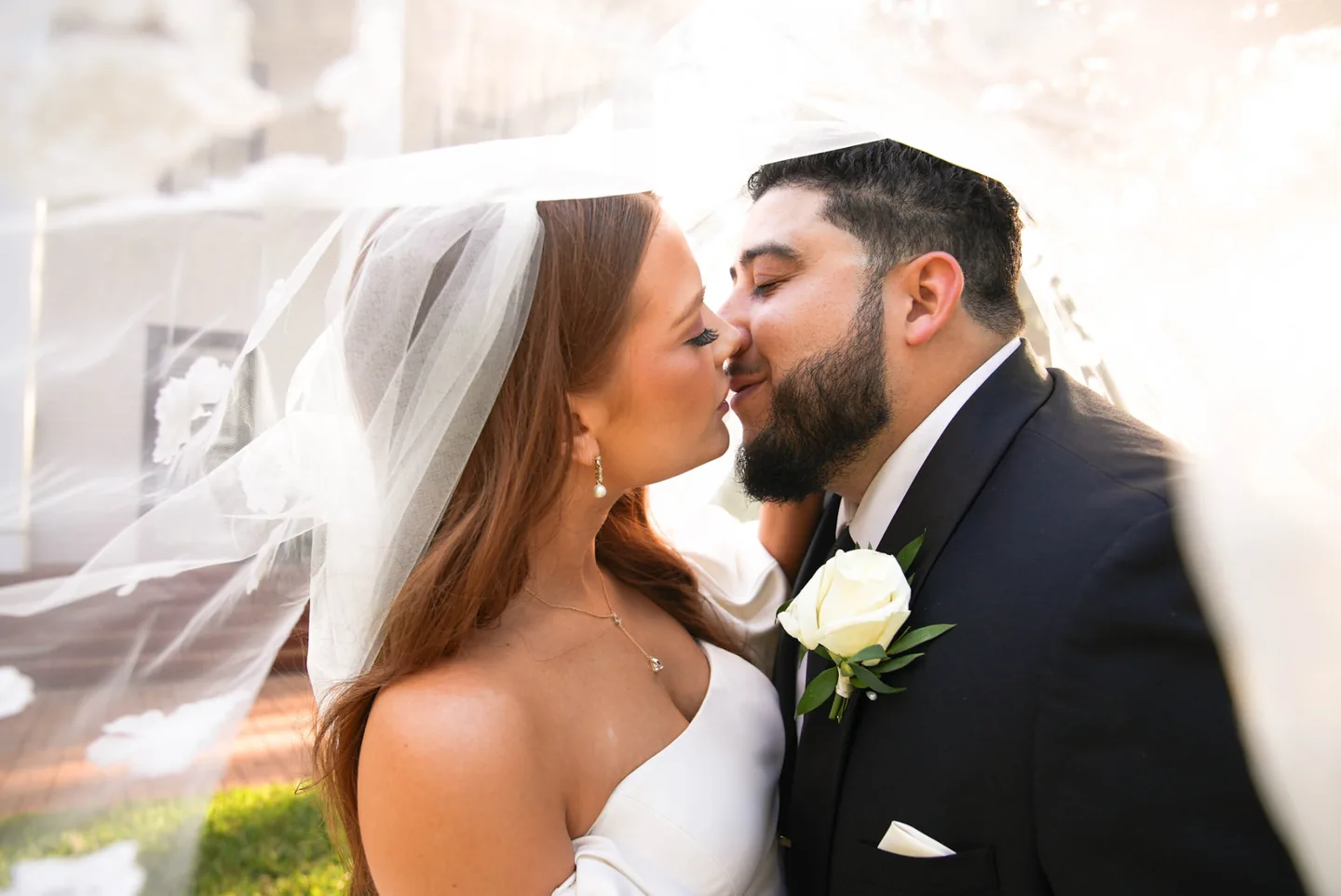 Bride and groom leaning in to kiss beneath a backlit veil