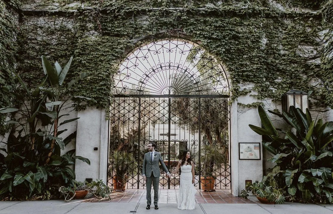 Bride and groom walking apart toward an ivy-covered iron gateway