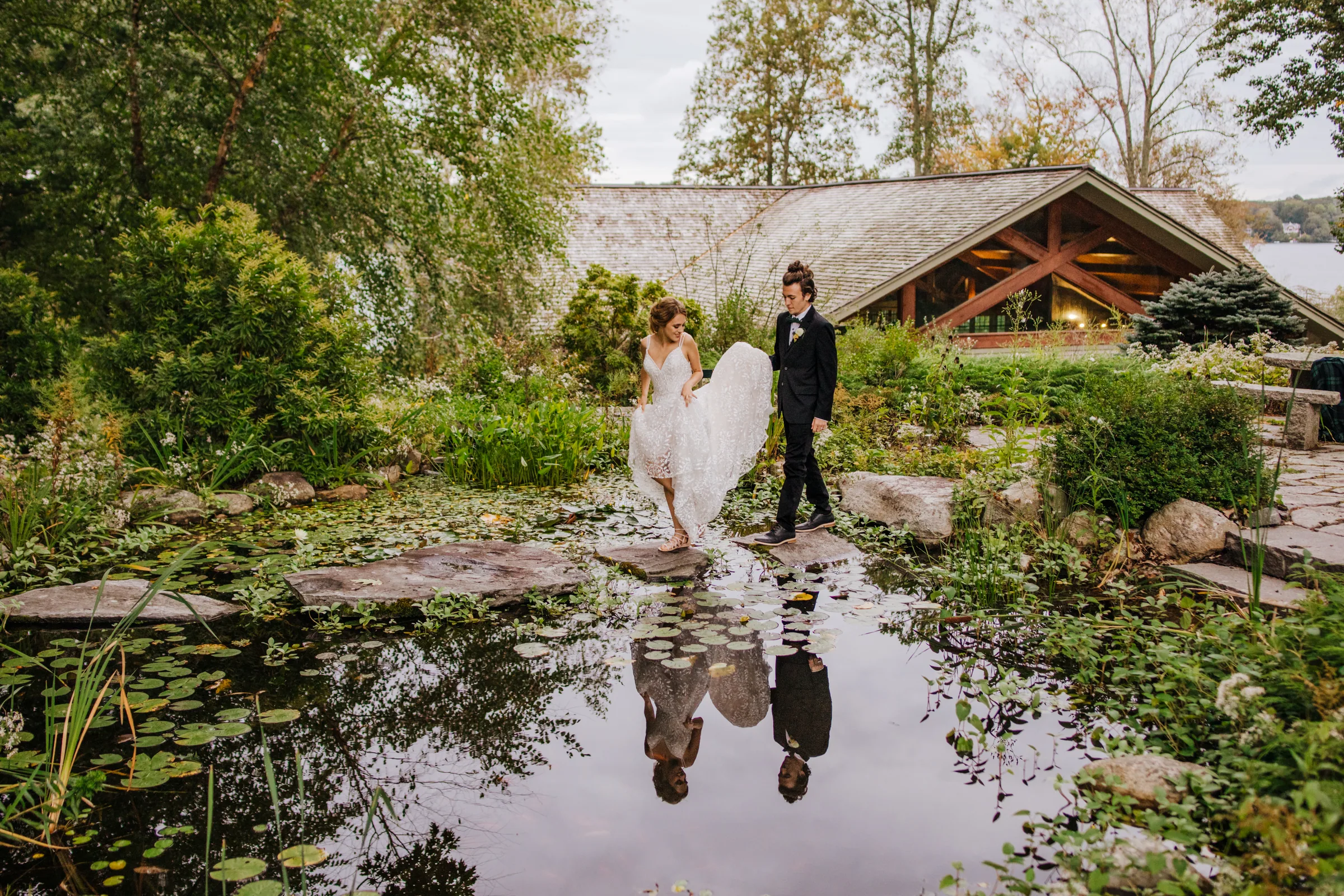 Bride and groom standing beside a garden pond, their reflection in the water