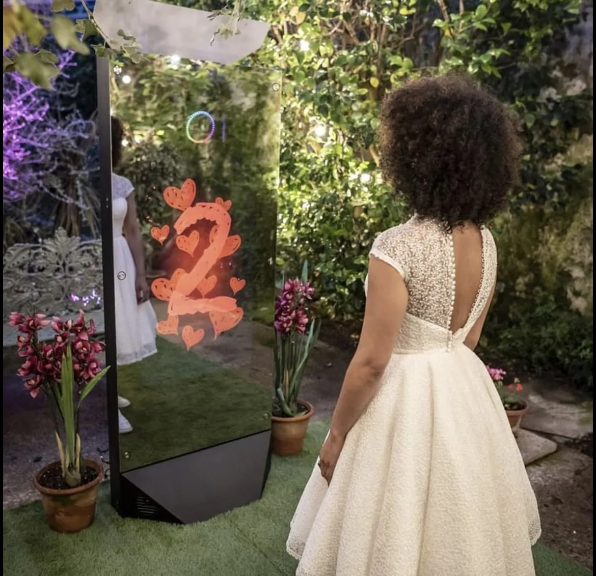 Guest in a gown posing in front of a mirror photo booth set up in a garden