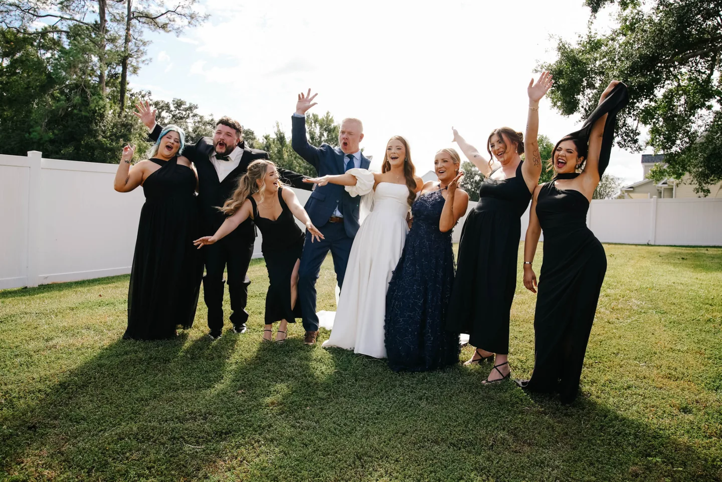 Wedding party cheering with arms raised on a sunlit lawn