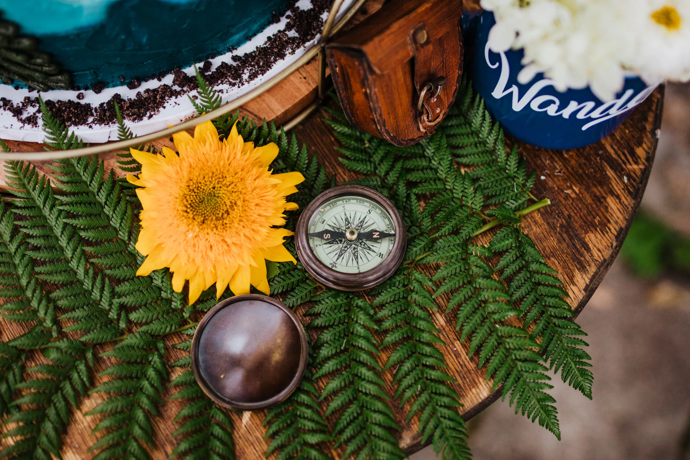 Wedding reception detail of a sunflower, ferns and a hand-lettered sign arranged on a table